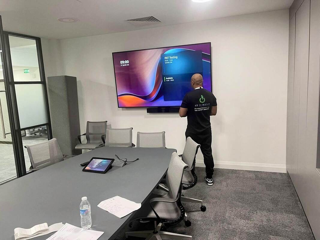 PAT Testing being conducted in a Buckinghamshire office by a PAT Testing engineer who is working on a large wall-mounted screen in a modern conference room.
